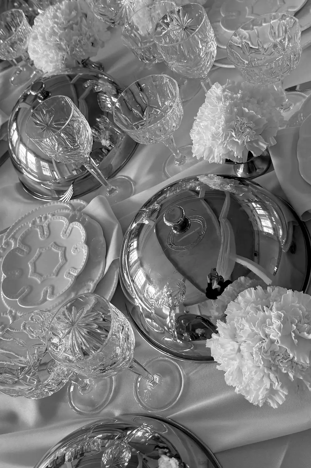 A black and white view of a set table with crystal glasses, porcelain dishes, and white flowers in an event space.