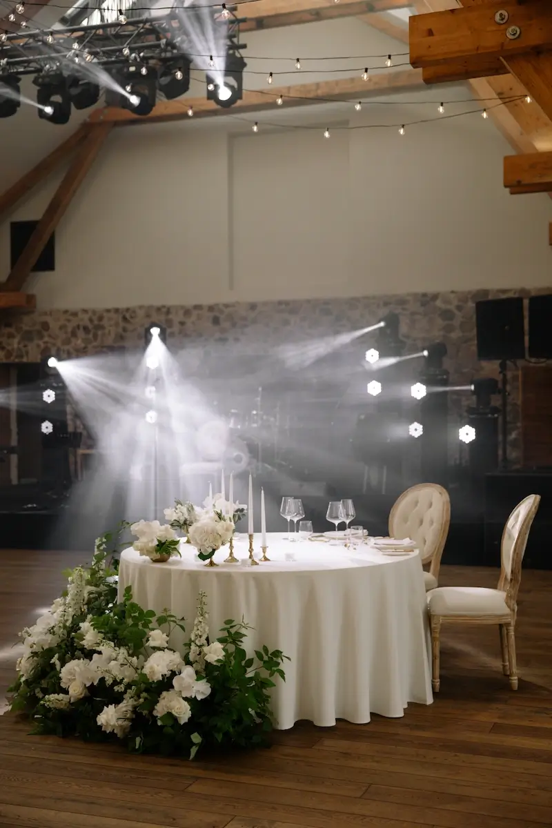 Round table with a white tablecloth, a flower arrangement, and candlesticks in a hall with stage lighting