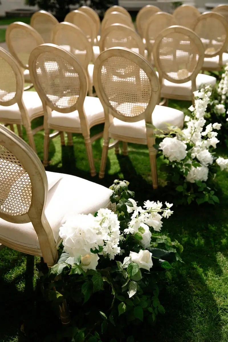 Chairs in rows for an outdoor event with white flower decorations on the lawn