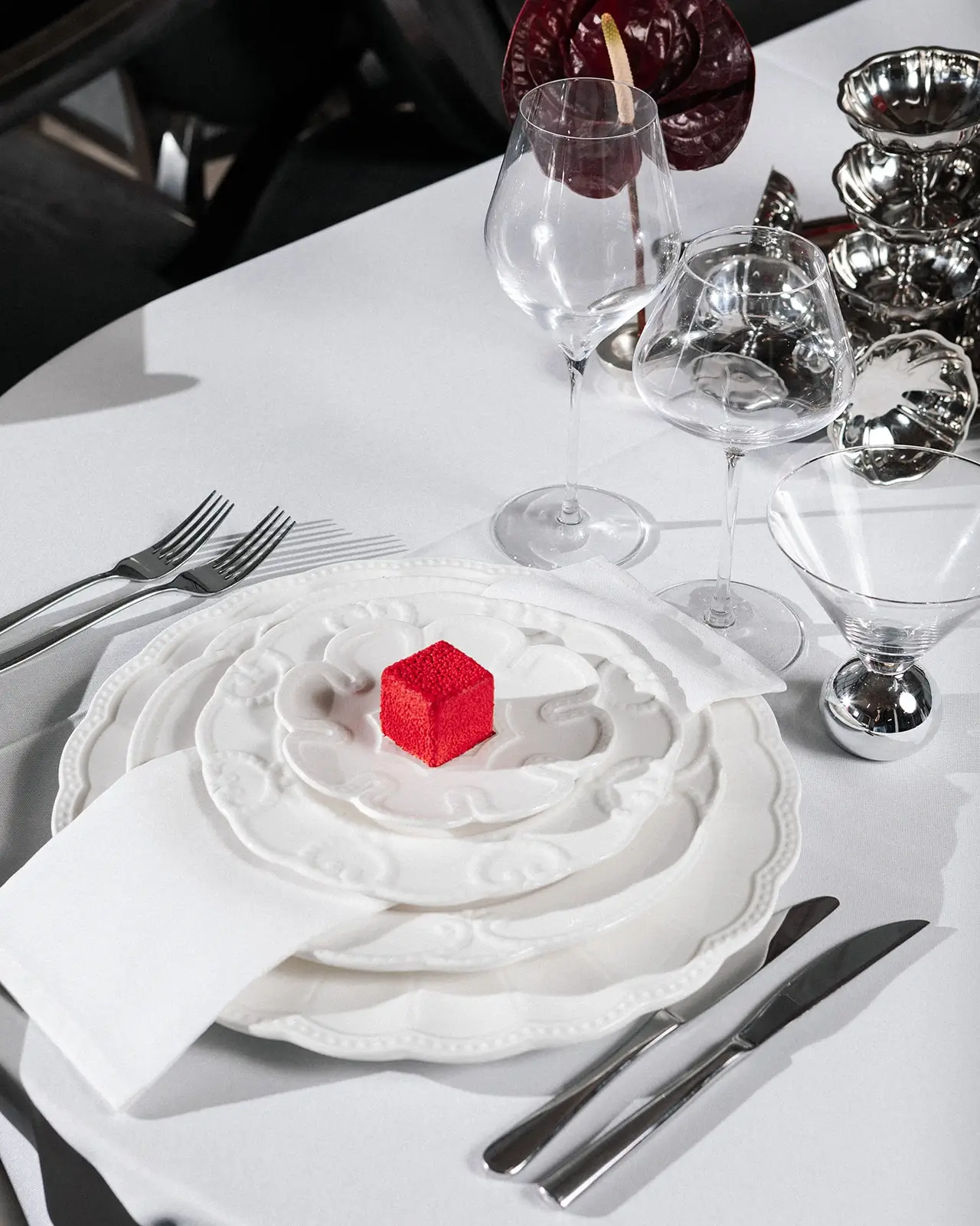 An elegantly set table with a white porcelain plate, glasses, and a small red dessert in an event space.