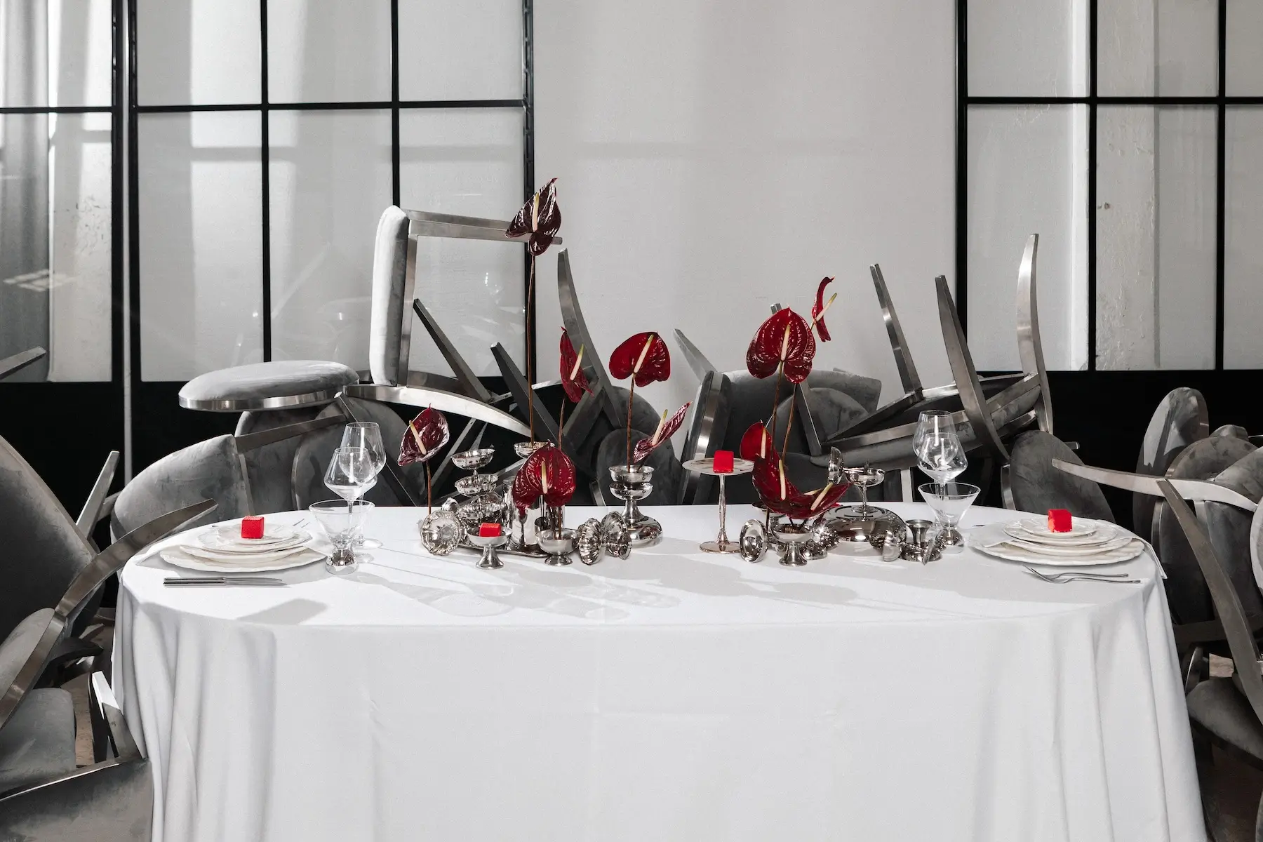 A long table with a white tablecloth, table setting, and red flower decorations in a spacious hall.