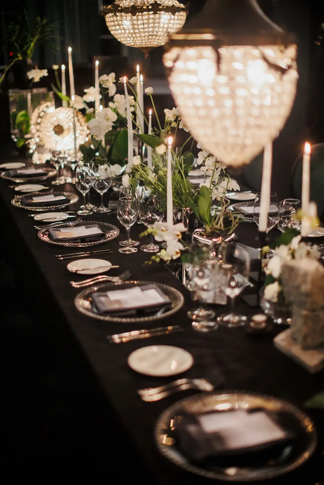 A long table for events with a black tablecloth, candles, glasses, plates, and flower decorations