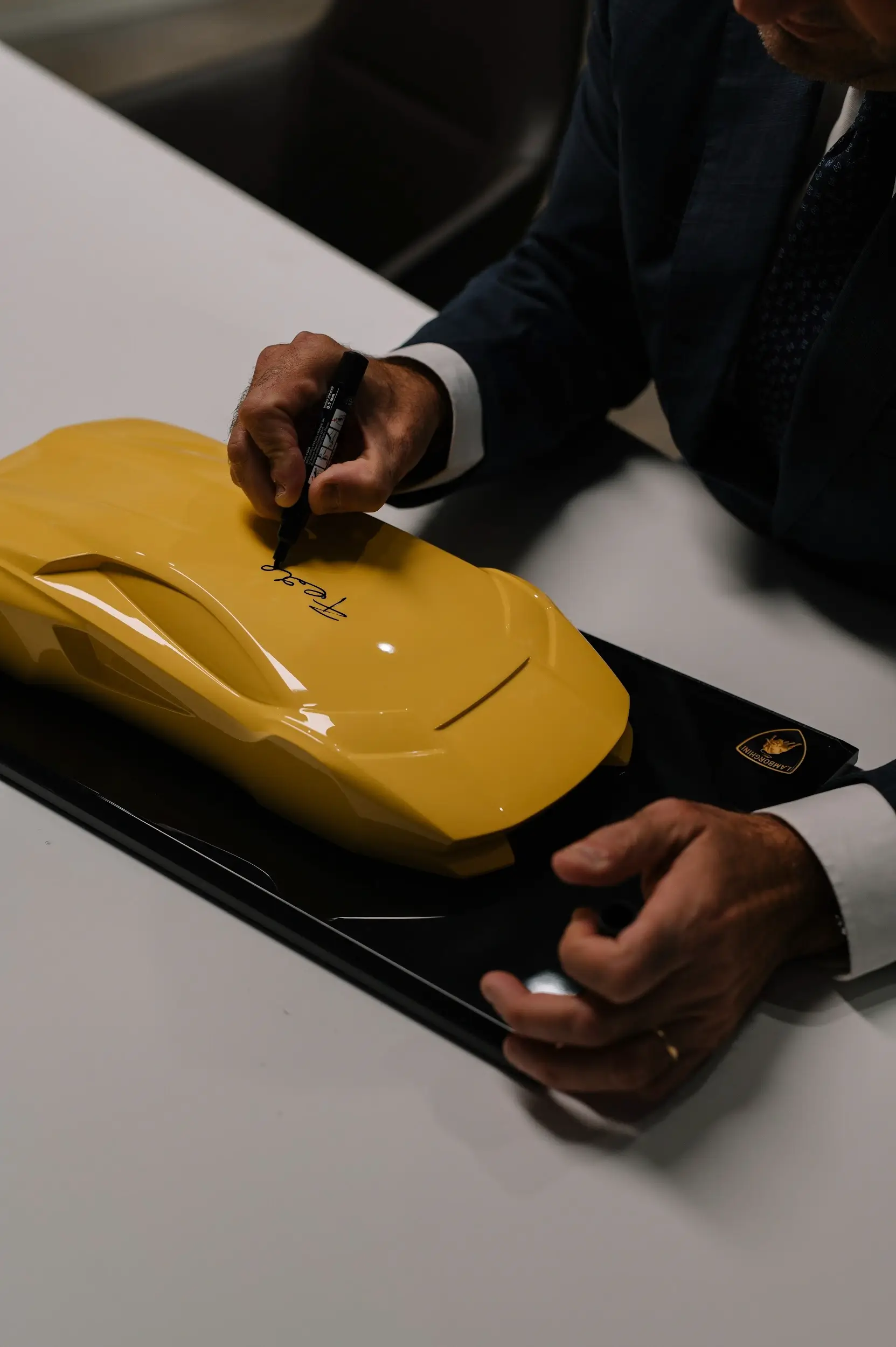 Man signs yellow Lamborghini car-shaped decoration on table