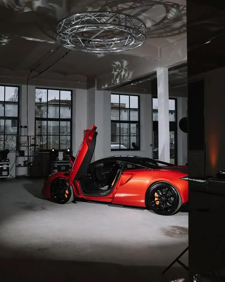 A sports car parked in a spacious event space with high ceilings, large windows, and professional lighting for a presentation.