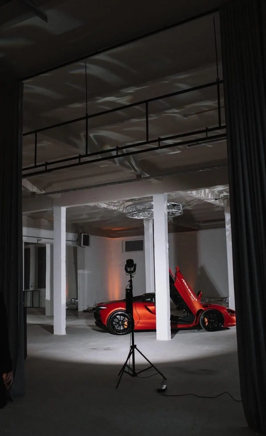 A sports car parked in a spacious indoor area with high ceilings, columns, and professional lighting for a photoshoot.