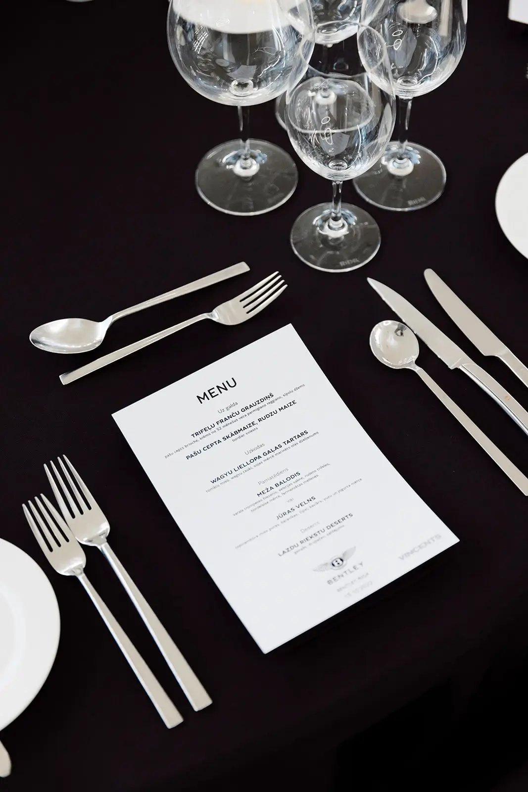 Table setting with a black tablecloth, a menu, glasses, and silver-colored cutlery