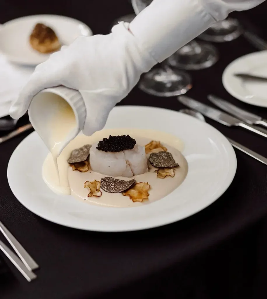 Elegantly plated dish being topped with a creamy sauce, with delicate details on the plate.